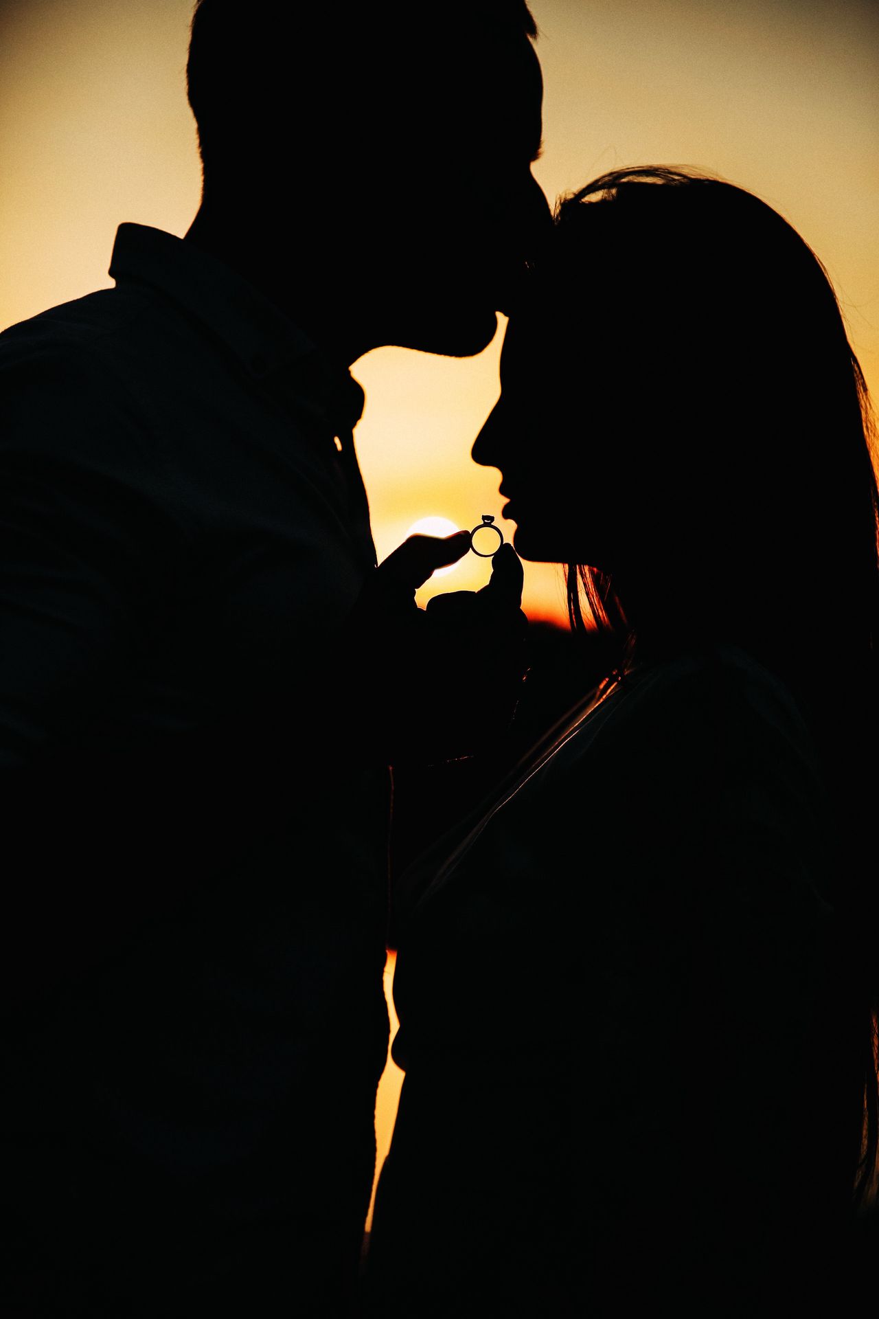 Silhouette of couple with engagement ring at sunset, symbolizing the brightest moment